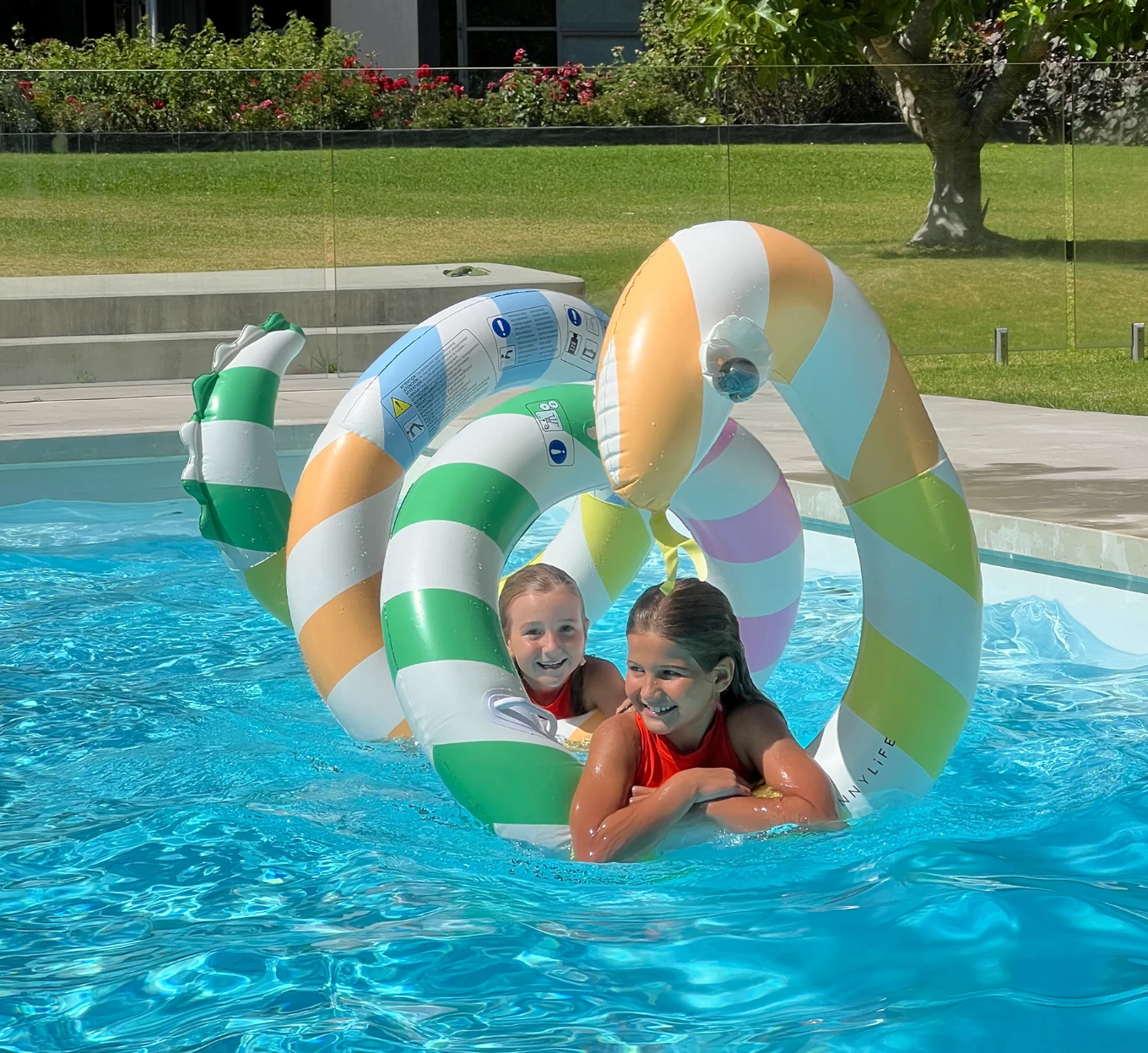 Two children playing in a pool with colorful inflatable rings.