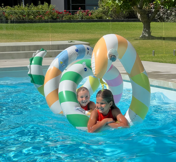 Two children playing in a pool with colorful inflatable rings.