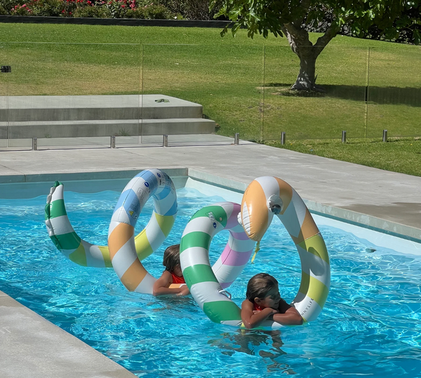 Two children playing with colorful inflatable rings in a pool.