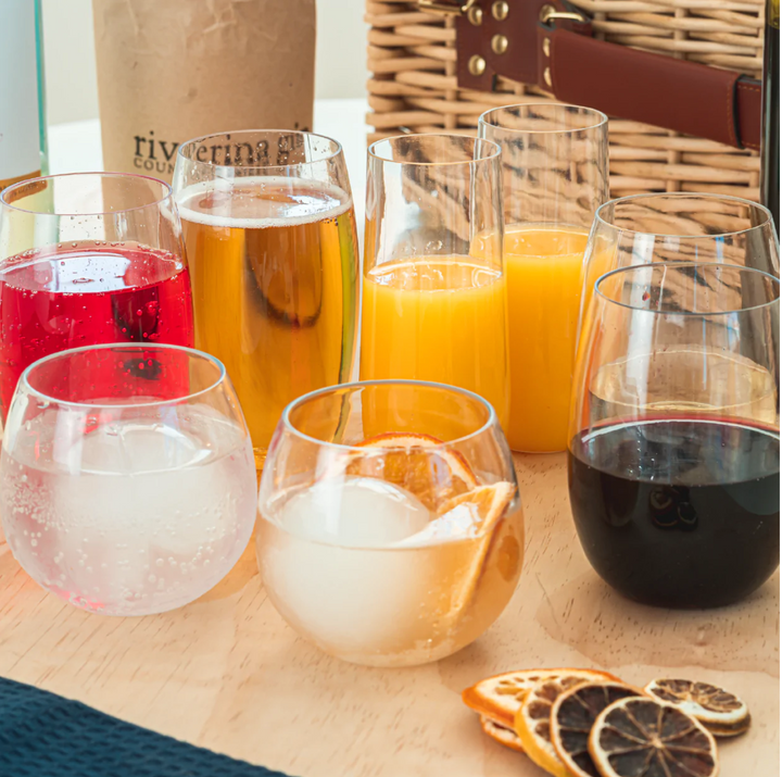 A collection of beach glasses in various sizes, including wine tumblers, beer schooners, and gin balloons, displayed on a table with a green drawstring bag.